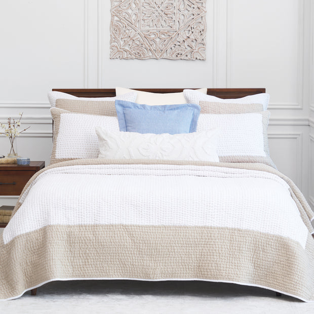 tan and white bedding paired with coordinating shams, blue pillow, and white embroidered oblong pillow